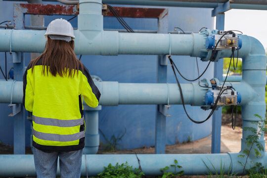 Female engineer inspecting water treatment pipelines with a digital tablet at a water supply plant. Concept of infrastructure, utility maintenance, water management and safety.