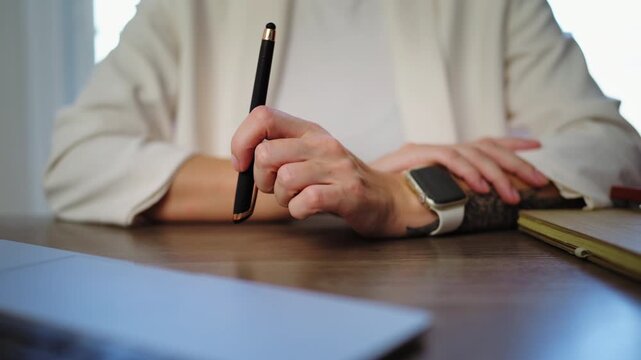 Close-up of businesswoman nervously fidgeting with a stylus at an office desk while thinking about a project, representing workplace stress, anxiety, pressure and challenging professional decisions.