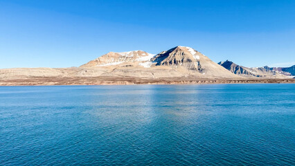 Majestic snow-capped mountain rising above a tranquil blue sea on a clear, sunny arctic day © HABI ANGGARA PUTRA