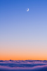Fototapeta premium Crescent moon shining in a vibrant twilight sky above a thick layer of soft rolling clouds
