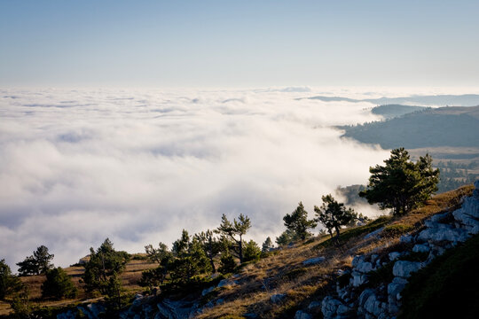 Breathtaking view of a dense sea of clouds rolling over a rugged mountain ridge at sunrise