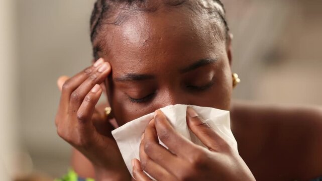 African woman blowing nose with a tissue feeling unwell with flu