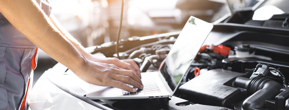 Professional car mechanic hands using laptop computer for diagnostic checking system and vehicle performance analysis during engine service maintenance in auto repair workshop garage.