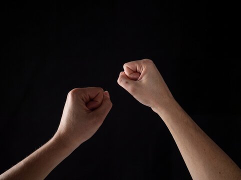 Close-up of two fists clenched and raised against black background symbolizing strength and determination