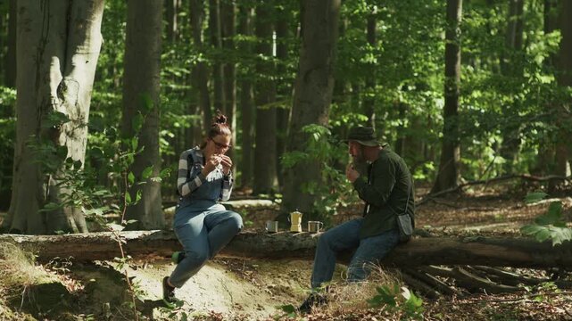 Couple Eating Sandwiches and Having Picnic on Tree Log in Forest