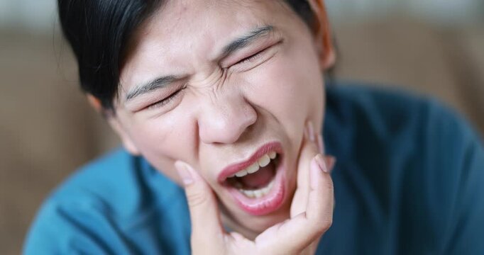 Woman suffering from toothache, holding her cheek in pain, tooth pain, dental problems, oral health, tooth sensitivity, cavity, dental treatment, and healthcare, close-up, Asian Thai people