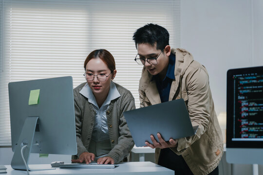 Asian software developers working together, analyzing code on computers, and discussing project strategy in a modern office environment