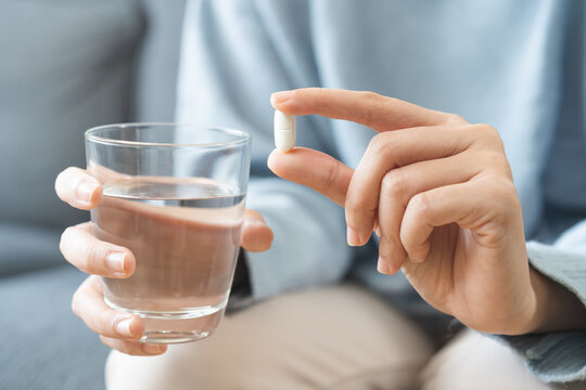 Sick, asian young woman, girl hand holding pill, painkiller medicine from stomach pain, headache, pain for treatment, take drug or vitamin and glass of water at home, pharmacy and health care concept.