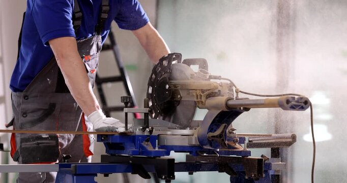 A craftsman expertly operates a miter saw, cutting wood pieces with precision in a bright workshop. Dust fills the air as each cut is made, showcasing skillful craftsmanship.