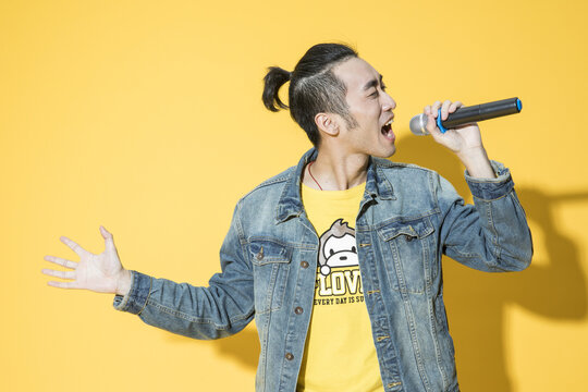 Passionate Young Asian Man Singing into Microphone Against Yellow Background