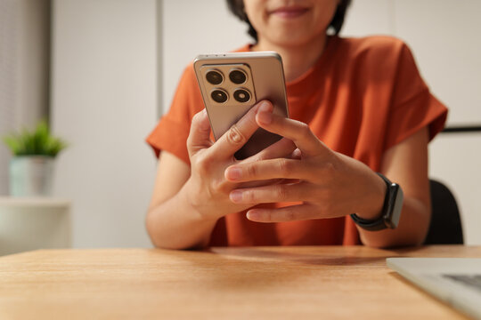 Asian Woman using a smartphone at a desk at home, representing mobile apps, online chatting, digital communication, social media and lifestyle.