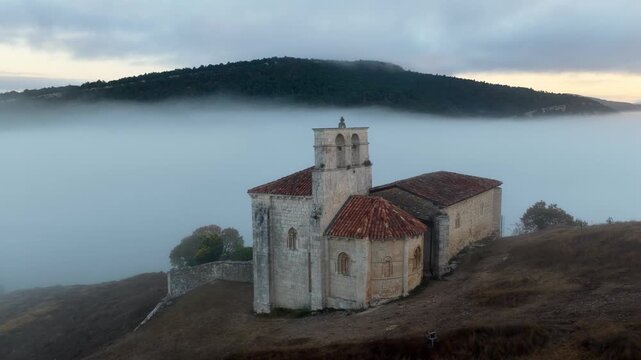 Peque&ntilde;a iglesia rom&aacute;nica de piedra construida sobre una colina rocosa con forma de barco al amanecer, con niebla en el Valle de Losa, Arquitectura medieval antigua, templo hist&oacute;rico rural, Pantale&oacute;n.