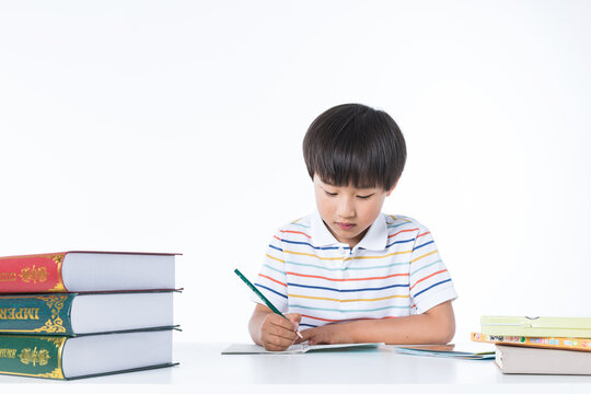 Young Boy Studying and Writing Homework at Desk with Books