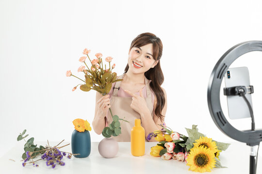 Female host live streaming a flower arrangement with smartphone and ring light