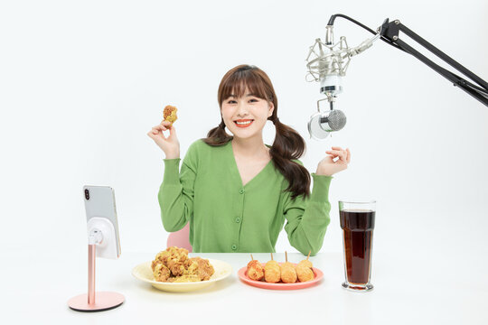 Cheerful young woman eating fried chicken during a live broadcast or mukbang
