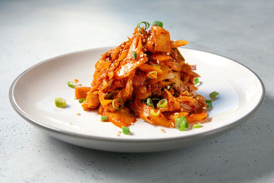 Spicy Korean kimchi made with fermented cabbage, chili seasoning, scallions and sesame seeds, served on a white plate