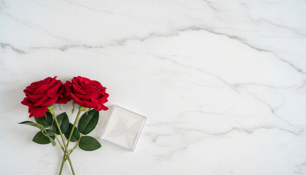 Two red roses and a gift box on a white marble surface