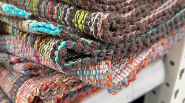Close up view of bundled heavy woven blankets or carpets with bright patterns. Traditional handmade home decor merchandise, authentic craft material backdrop, cozy winter design.