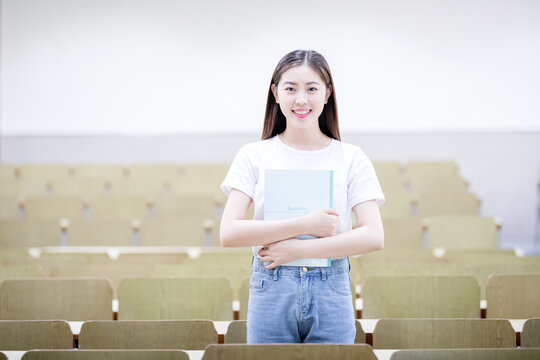 Smiling Female Student Holding Notebook in Empty Lecture Hall