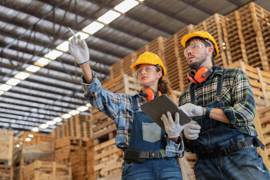 Workers discuss tasks in a warehouse with pallets stacked high in the background