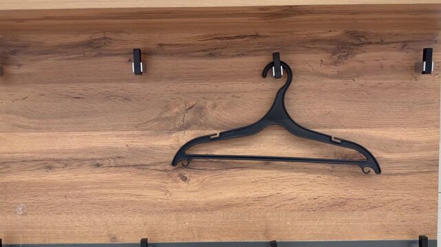 Black plastic clothes hanger hanging swinging on a wooden wall hook. Wardrobe organization, clothing storage, minimalist home interior. Metaphor of emptiness, waiting, and loneliness.