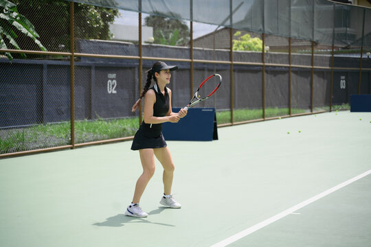 Asian Woman Playing Tennis on Outdoor Court in Black Sportswear with Racket Ready Position