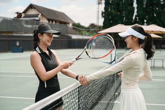 Two Asian Female Tennis Players Meet at the Net with a Handshake Before or After an Outdoor Match