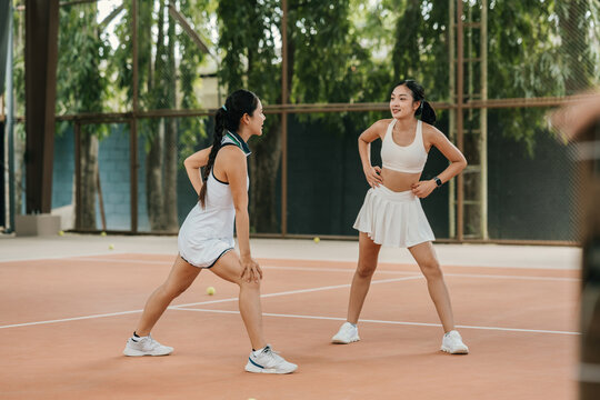 Two Asian friends Warming Up and Stretching Together on an Indoor Tennis Court Before Playing