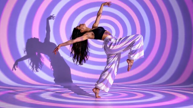 Woman dancing with arms raised against a purple and pink concentric circle background with woman long