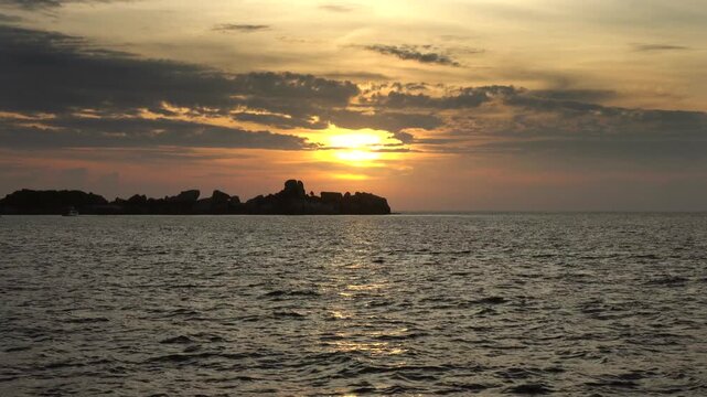 View of the Similan Islands silhouette against a golden sunset over the Andaman Sea in Lam Kaen, Phang Nga, Thailand.