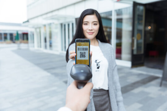 Young woman showing QR code on smartphone for scanning outdoors