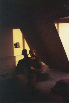 Man sitting on bed illuminated by dramatic afternoon window light