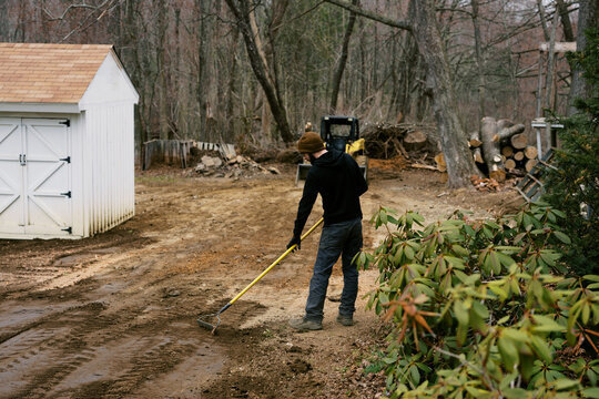 man raking soil that was leveled out in a rural backyard in spring