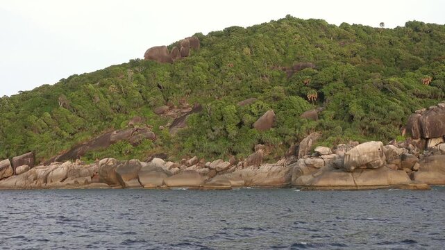 View of Similan Islands coastline featuring lush green hills and large granite boulders along the sea in Lam Kaen, Phang Nga, Thailand.