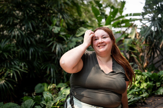 A redhead Gen-Z girl smiles in a tropical garden in Bangkok