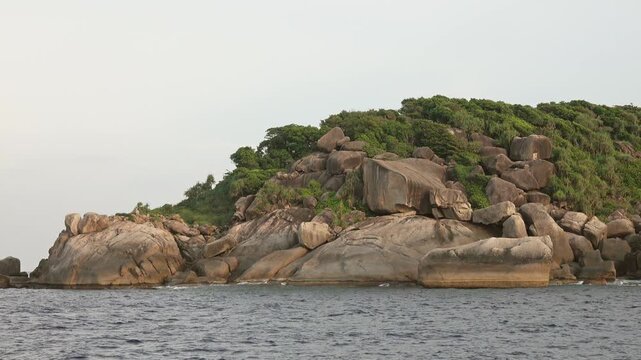 View of the rocky coastline of the Similan Islands with lush green vegetation and large granite boulders meeting the sea in Lam Kaen, Phang Nga, Thailand.