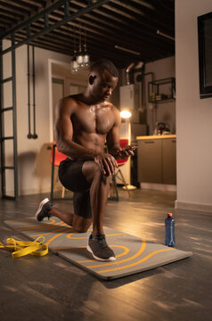 Lunging black sportsman using mobile phone during training at home