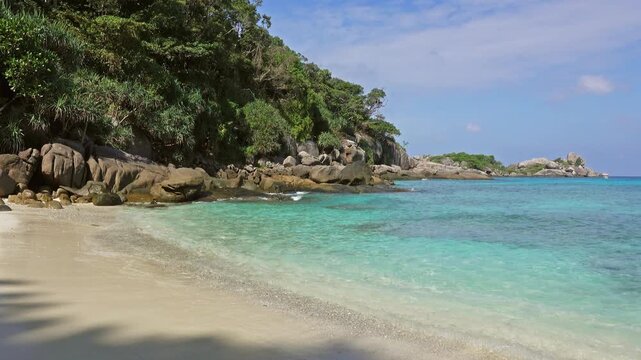 View of Similan Islands beach with turquoise water, rocky coastline, and lush tropical vegetation in Lam Kaen, Phang Nga, Thailand.