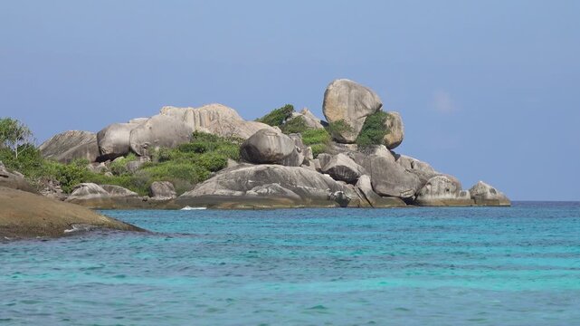 View of large granite boulders on the coast of the Similan Islands with turquoise water and lush tropical vegetation in Lam Kaen, Phang Nga, Thailand.
