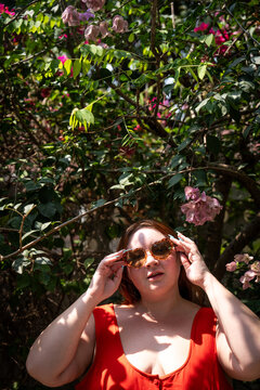 Portrait of a plus-size Gen Z model wearing sunglasses beneath a tree