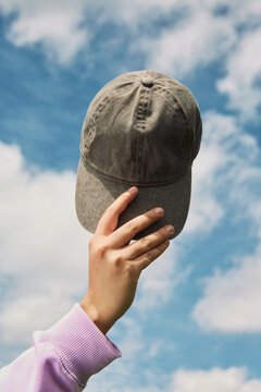 Hand holding baseball cap against blue sky