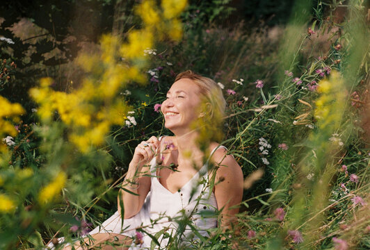 A woman sits laughing among summer wildflowers in a meadow