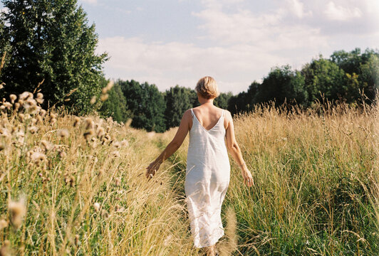 A woman stands in tall summer grass beneath an open sky