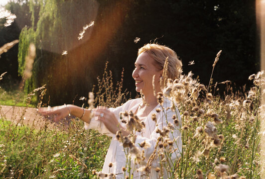 A woman releases dandelion seeds into a sunlit meadow