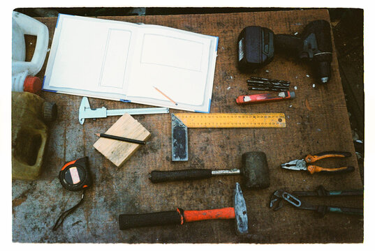 Hand tools, drill and building plans arranged on a workbench