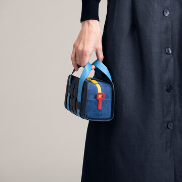 Hand Holding Blue Bag Beside Black Coat