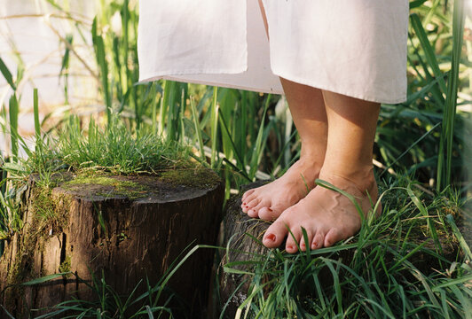 A woman balances barefoot on an old stump among reeds