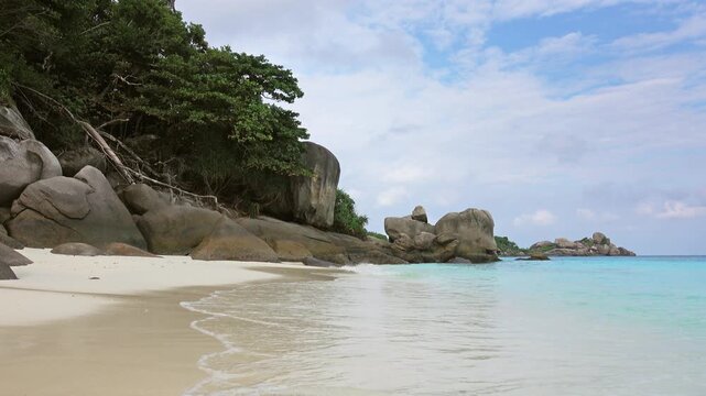 View of the white sand beach and large granite boulders at Similan Islands with lush green vegetation and turquoise sea in Lam Kaen, Phang Nga, Thailand.
