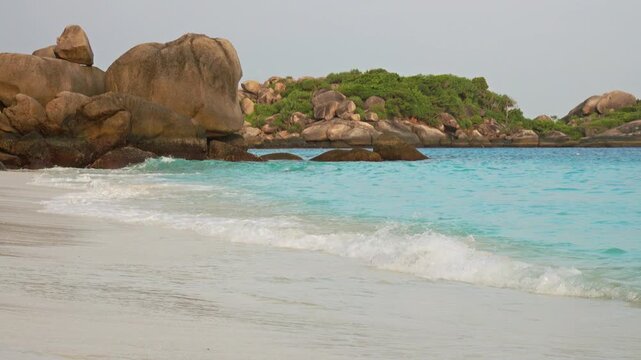 View of the turquoise waters and white sandy beach of the Similan Islands with large granite boulders and lush tropical vegetation in Lam Kaen, Phang Nga, Thailand.