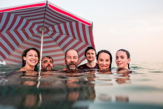 Smiling friends swimming in the sea with beach umbrella
